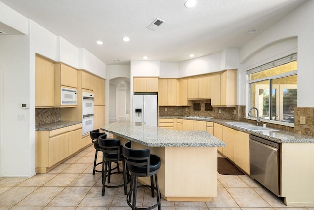 kitchen with a kitchen island, sink, white appliances, light tile patterned floors, and light brown cabinetry