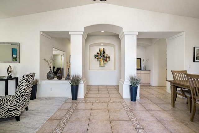 foyer entrance featuring decorative columns, light tile patterned floors, and vaulted ceiling