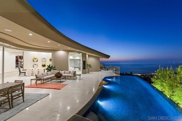 pool at dusk featuring a patio area, a water view, and outdoor lounge area