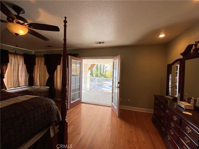 bedroom featuring a textured ceiling, wood finished floors, visible vents, baseboards, and access to exterior