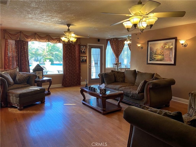 living area with light wood-type flooring, ceiling fan, a textured ceiling, and baseboards