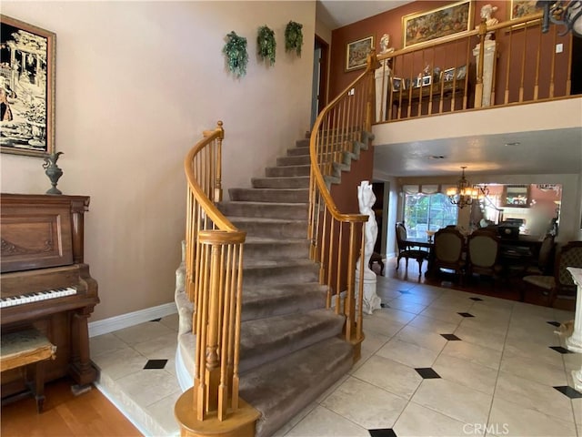 stairway featuring a towering ceiling, an inviting chandelier, baseboards, and tile patterned floors