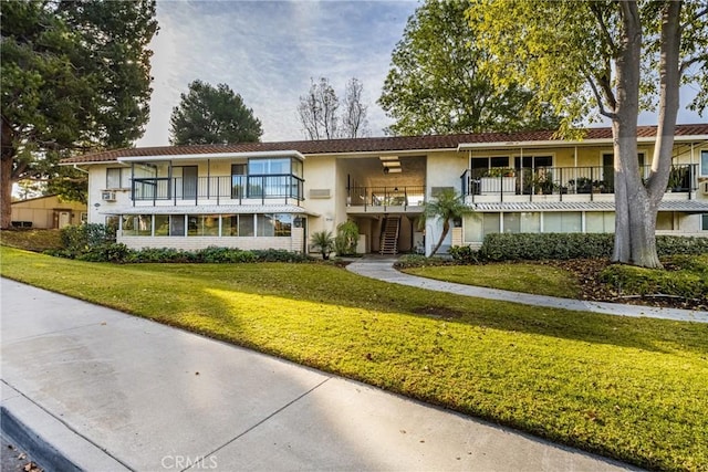 view of front of home with a balcony, stucco siding, a front lawn, and stairway