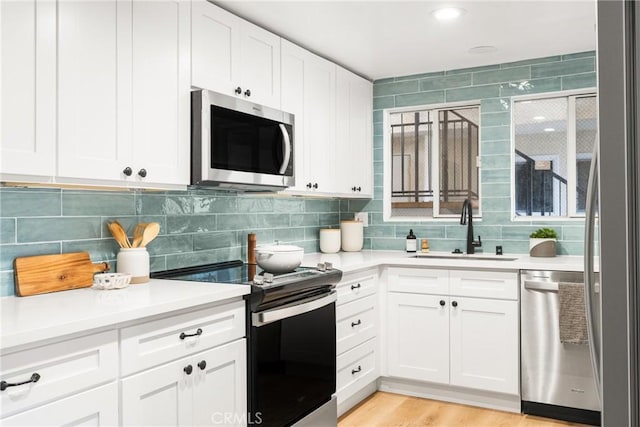 kitchen with white cabinets, a sink, light countertops, stainless steel appliances, and tasteful backsplash