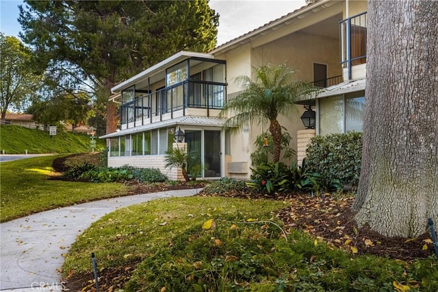 back of property featuring a balcony, a lawn, and stucco siding