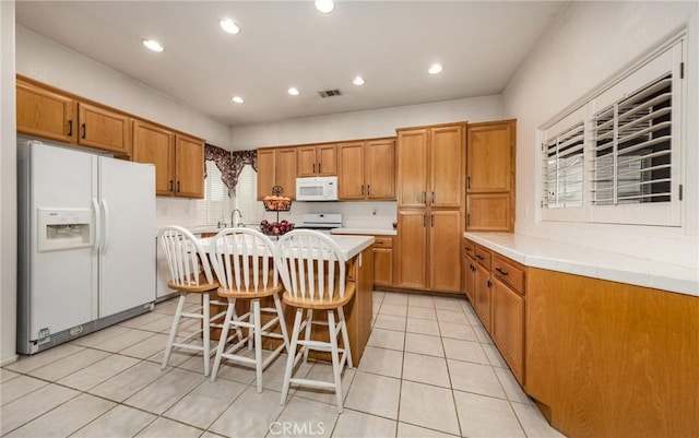 kitchen featuring a breakfast bar, a kitchen island with sink, light tile patterned floors, and white appliances