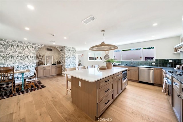 kitchen with wallpapered walls, light wood finished floors, visible vents, stainless steel appliances, and a sink