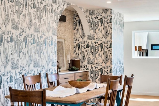 dining room featuring arched walkways, baseboards, and wood finished floors