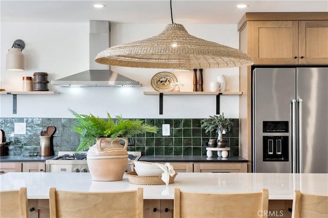 kitchen with decorative backsplash, hanging light fixtures, high end fridge, and wall chimney exhaust hood