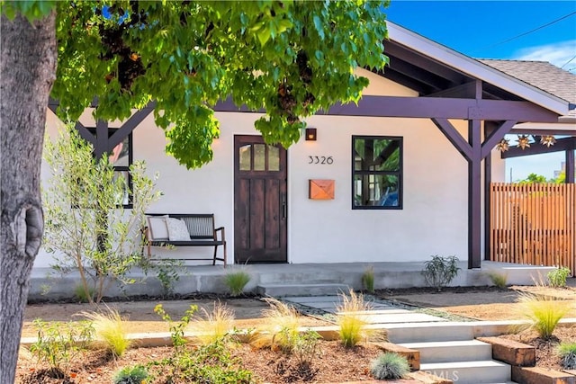 view of exterior entry with fence, a porch, and stucco siding