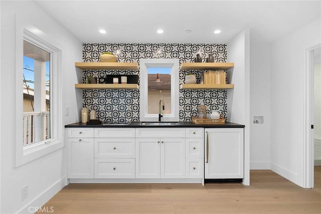 bar with decorative backsplash, sink, white cabinetry, and light hardwood / wood-style flooring