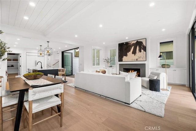 living room featuring sink, beamed ceiling, and light wood-type flooring