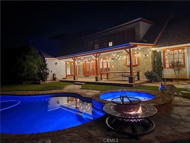 pool at night with an outdoor fire pit, an in ground hot tub, and a patio