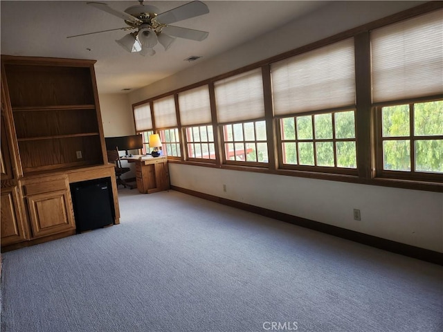 unfurnished office with ceiling fan, light carpet, and built in desk