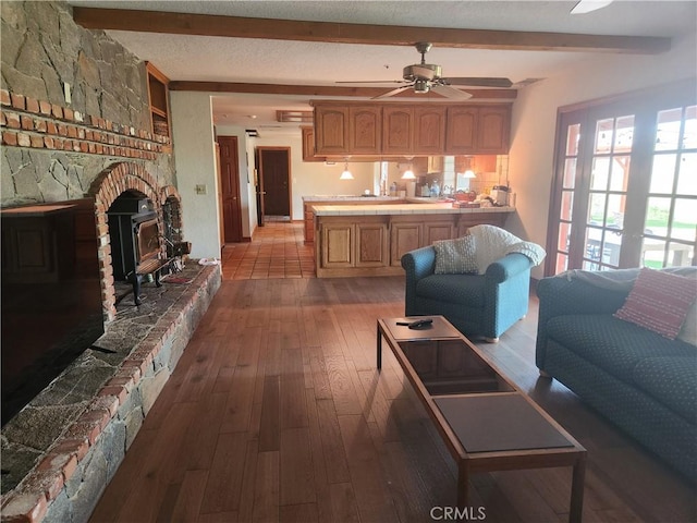 living room with ceiling fan, beam ceiling, a wood stove, and light hardwood / wood-style floors