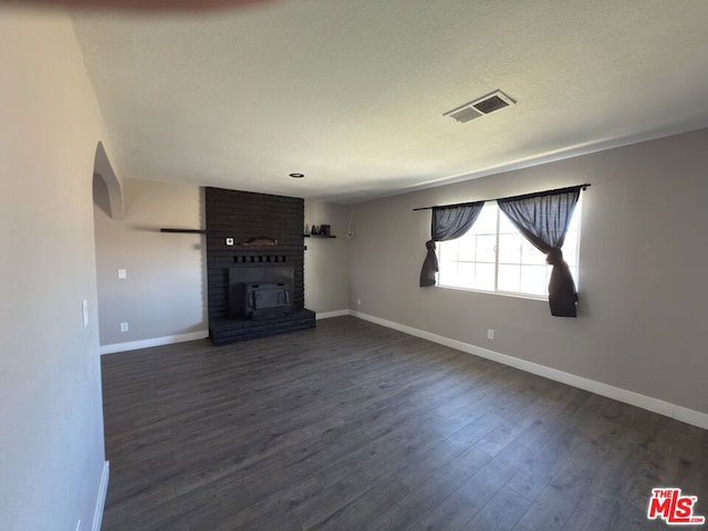 unfurnished living room featuring dark wood-type flooring, a textured ceiling, and a brick fireplace