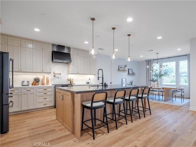 kitchen with wall chimney exhaust hood, white cabinetry, hanging light fixtures, a large island, and light hardwood / wood-style floors