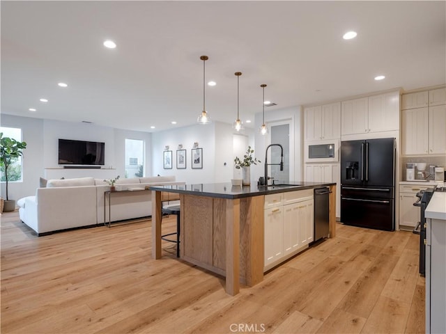 kitchen with white cabinetry, an island with sink, sink, and high end black refrigerator