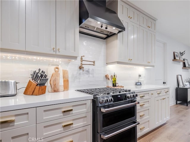 kitchen featuring wall chimney range hood, stainless steel range, light wood-type flooring, and decorative backsplash