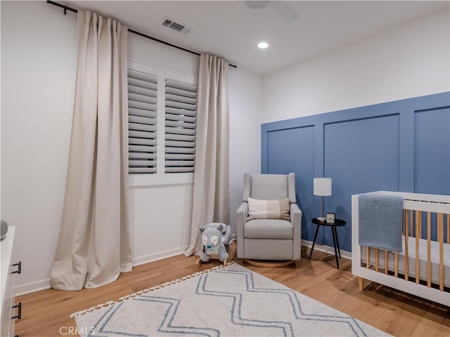 bedroom with hardwood / wood-style flooring, a nursery area, and ceiling fan