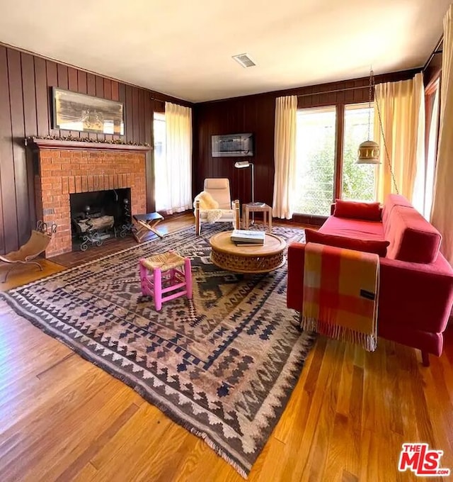 living room featuring wood-type flooring, a brick fireplace, and wooden walls