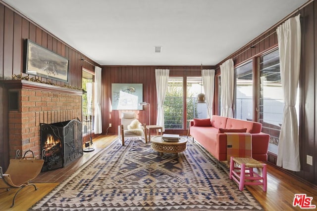 living room with a brick fireplace, hardwood / wood-style flooring, and wooden walls