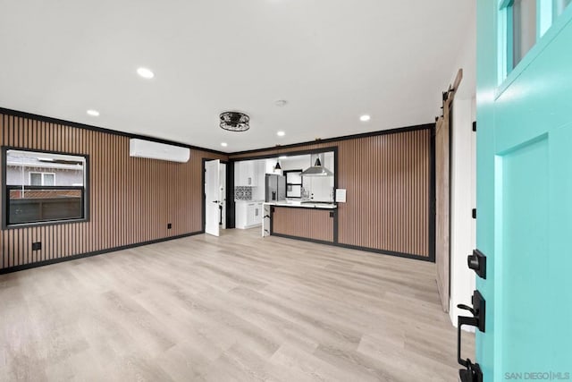 unfurnished living room featuring ornamental molding, a barn door, light hardwood / wood-style floors, and a wall mounted air conditioner