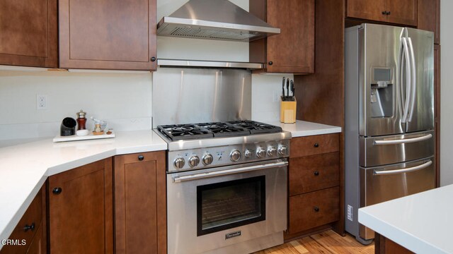 kitchen featuring light wood-type flooring, wall chimney range hood, and stainless steel appliances