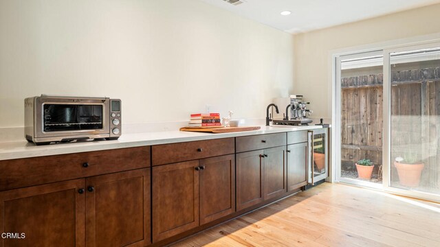 interior space featuring dark brown cabinets, light hardwood / wood-style floors, and beverage cooler