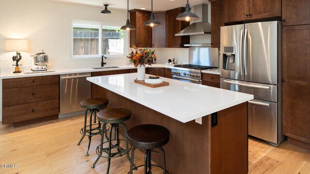 kitchen featuring a center island, sink, wall chimney exhaust hood, decorative light fixtures, and appliances with stainless steel finishes