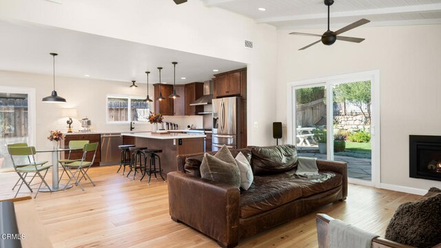 living room featuring ceiling fan, lofted ceiling with beams, light wood-type flooring, and sink