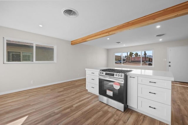 kitchen featuring white cabinets, stainless steel gas range, a center island, beamed ceiling, and light hardwood / wood-style flooring