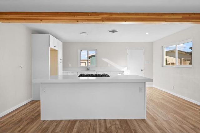 kitchen with a kitchen island, beamed ceiling, white cabinetry, light wood-type flooring, and gas stovetop