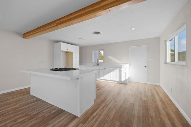 kitchen featuring sink, white cabinets, stainless steel gas stovetop, and beamed ceiling