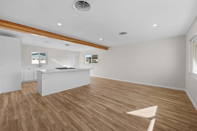 kitchen featuring white cabinetry, light hardwood / wood-style floors, gas cooktop, a kitchen island, and beamed ceiling