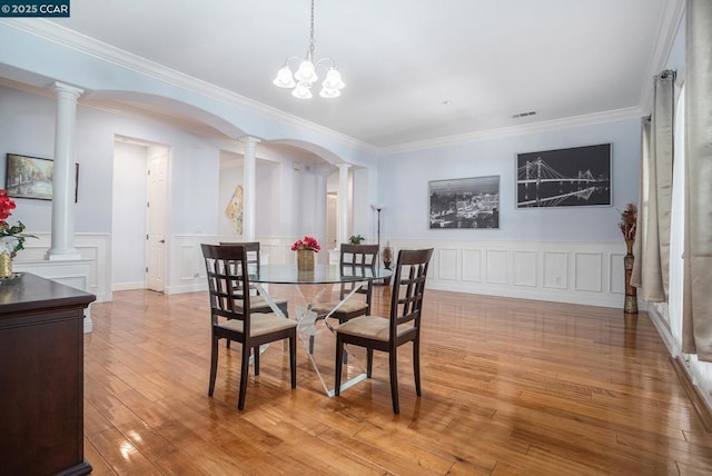 dining space with light hardwood / wood-style flooring, a notable chandelier, ornamental molding, and decorative columns