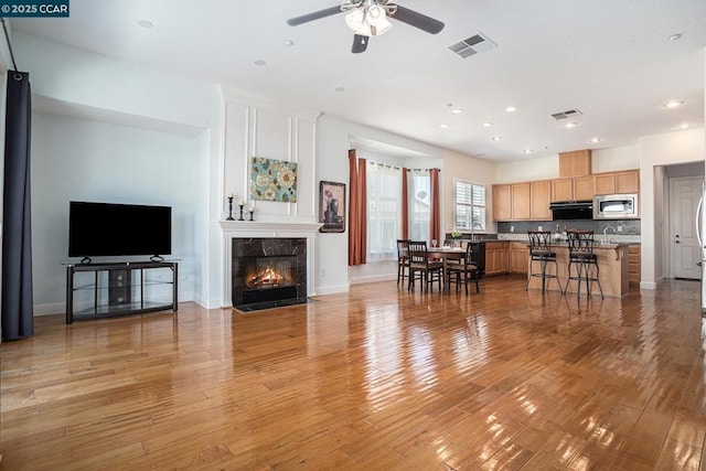 living room with a premium fireplace, light hardwood / wood-style floors, and ceiling fan