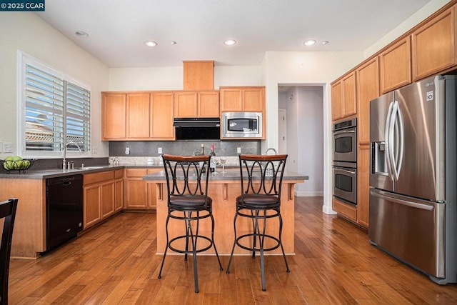 kitchen with appliances with stainless steel finishes, decorative backsplash, a center island, a kitchen breakfast bar, and sink