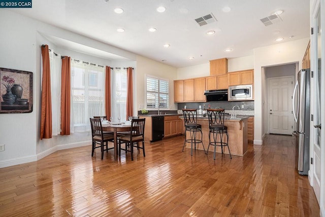 kitchen featuring extractor fan, an island with sink, appliances with stainless steel finishes, backsplash, and light wood-type flooring