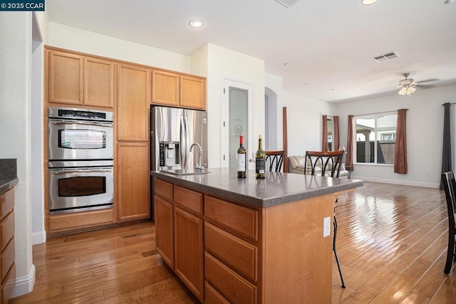 kitchen with a center island with sink, ceiling fan, appliances with stainless steel finishes, wood-type flooring, and sink