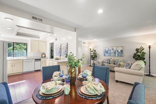 dining space featuring sink, a tray ceiling, and light hardwood / wood-style flooring