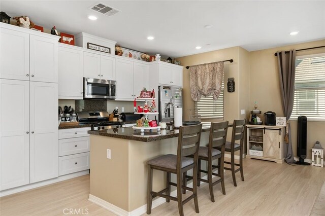 kitchen featuring appliances with stainless steel finishes, light hardwood / wood-style flooring, white cabinetry, and a kitchen island with sink