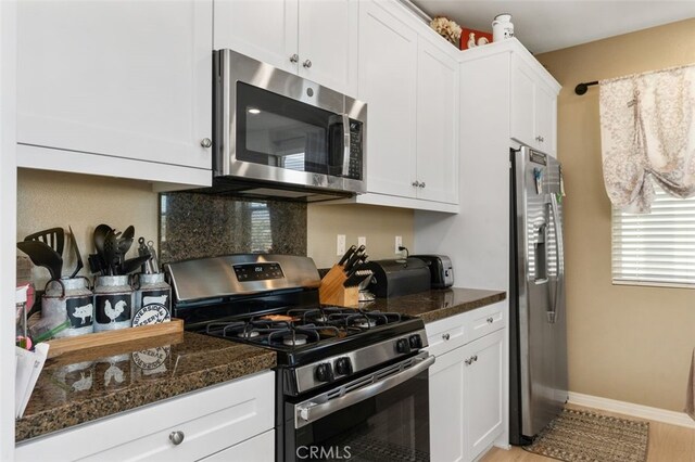 kitchen featuring appliances with stainless steel finishes, dark stone countertops, and white cabinetry