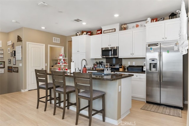 kitchen featuring white cabinetry, appliances with stainless steel finishes, decorative backsplash, a kitchen island with sink, and a breakfast bar