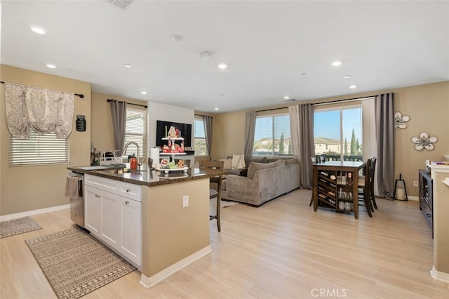 kitchen featuring a kitchen bar, white cabinetry, light wood-type flooring, a kitchen island with sink, and dark stone counters