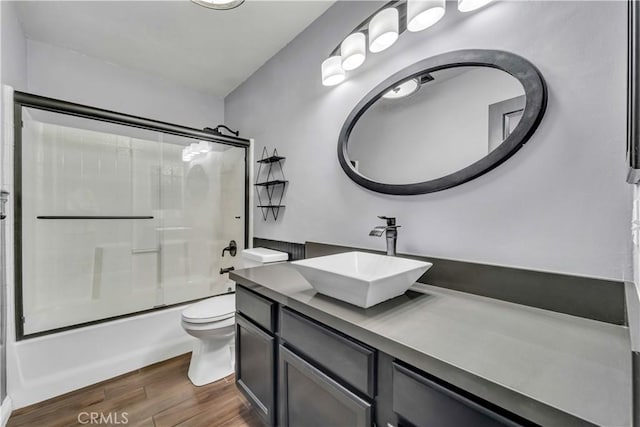 full bathroom with toilet, enclosed tub / shower combo, hardwood / wood-style floors, and vanity