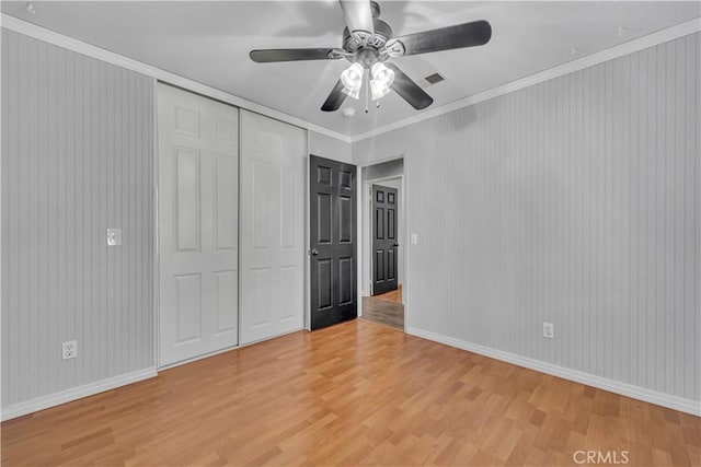 unfurnished bedroom featuring ceiling fan, a closet, crown molding, and hardwood / wood-style floors