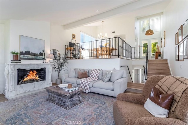 living room featuring beamed ceiling, plenty of natural light, a high end fireplace, and a notable chandelier