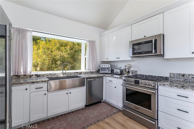 kitchen featuring vaulted ceiling, appliances with stainless steel finishes, stone countertops, white cabinetry, and sink