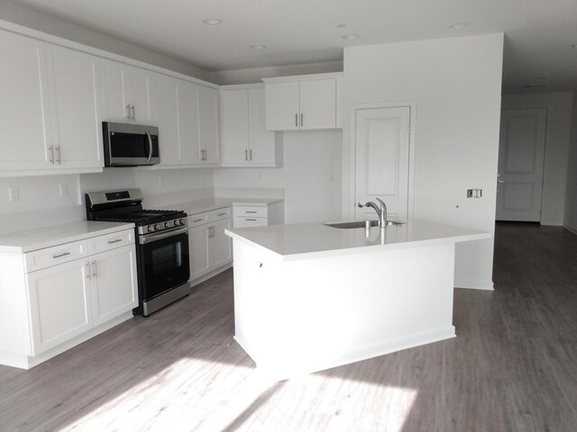 kitchen with white cabinets, appliances with stainless steel finishes, light hardwood / wood-style flooring, and a kitchen island with sink